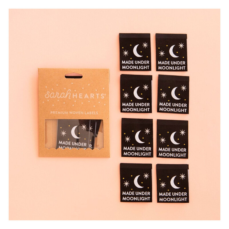 A package of Made Under Moonlight Sew In Labels next to 8 individual labels on a pink background to show scale and detail.