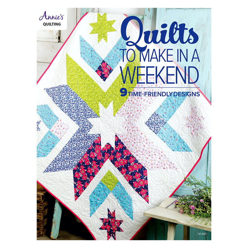 The front of the Quilts To Make In A Weekend book showing one of the completed quilts hung on a blue wooden ladder with a bouquet peeking out of the bottom right of the frame.
