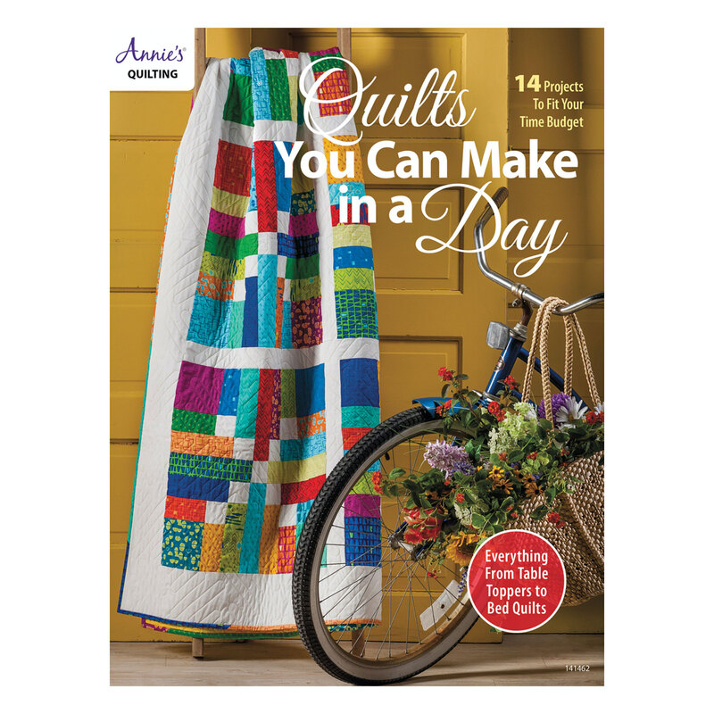 The front of the Quilts You Can Make in a Day book with one of the completed quilts displayed on a ladder against a golden brown wall next to a bicycle with a basket full of flowers hanging from the handlebars.