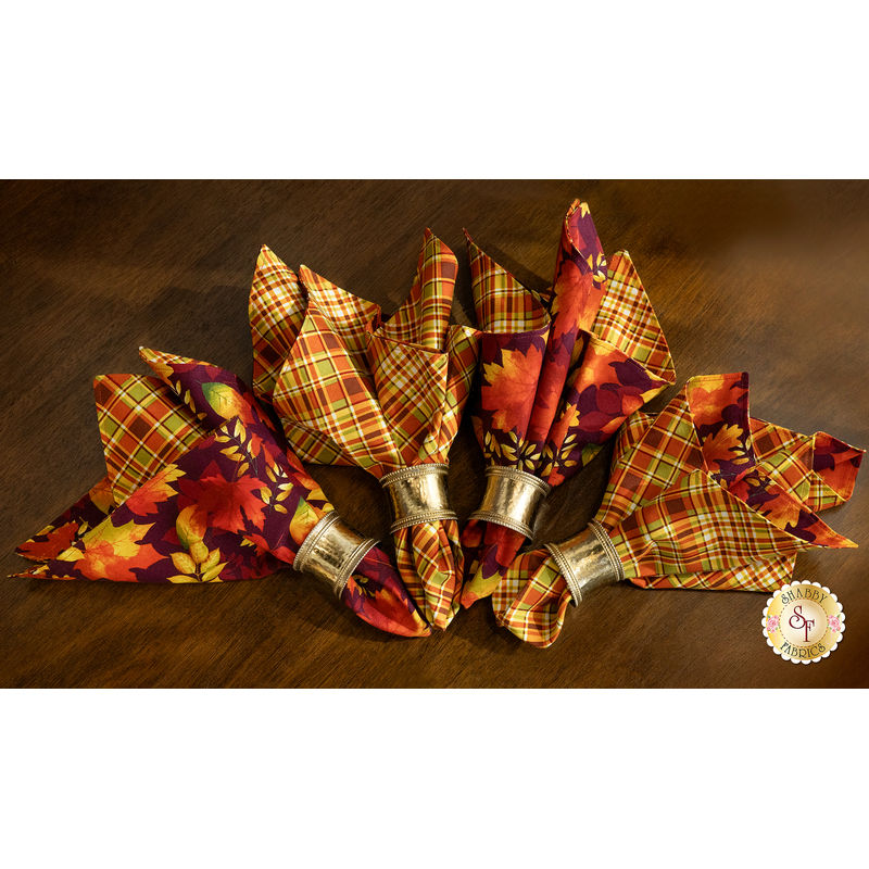 A top down shot of four cloth napkins in four metal napkin rings, fanned out on a dark wood table.