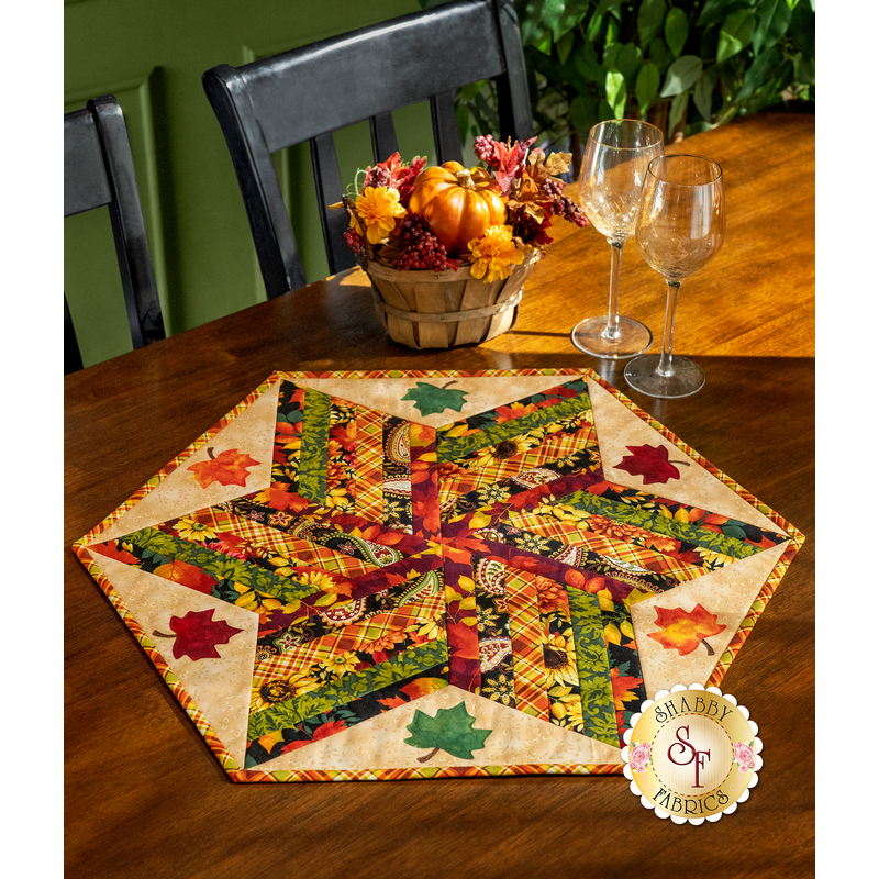 A hexagonal quilted table centerpiece project featuring autumn colors and applique leaves, and a basket of decorative fall items.