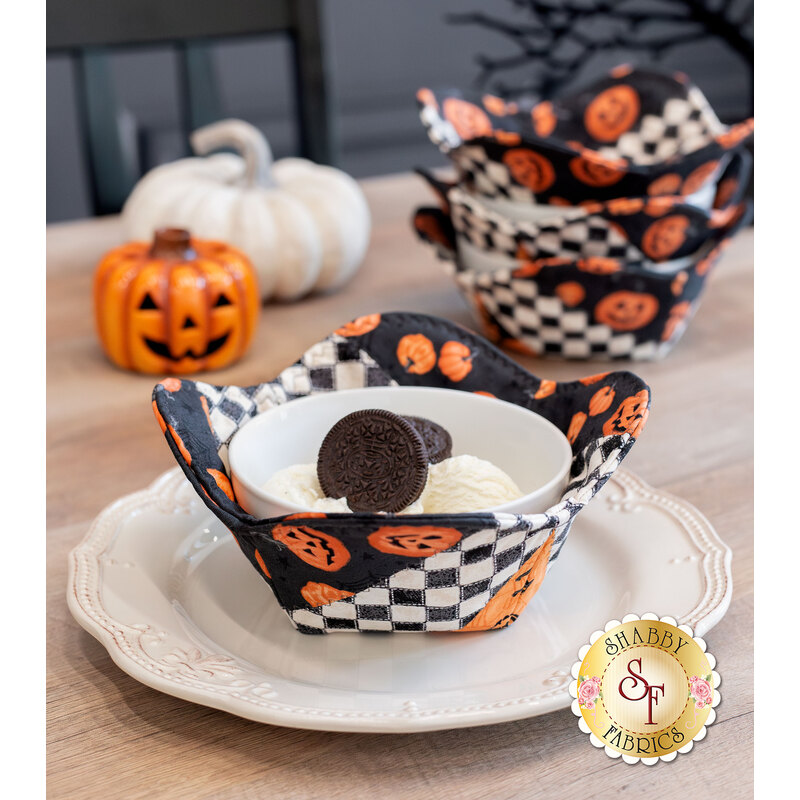 A decorative fabric bowl with ice cream and cookies, set against a backdrop of coordinating decor like pumpkins and three other bowl cozies.