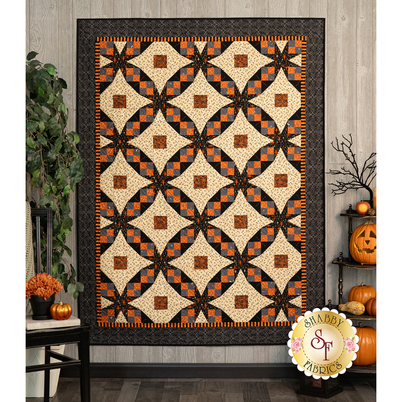 The completed Tennessee Waltz Quilt featuring a geometric pattern in orange, black, and cream fabrics from the Nevermore collection, displayed with autumn decor.