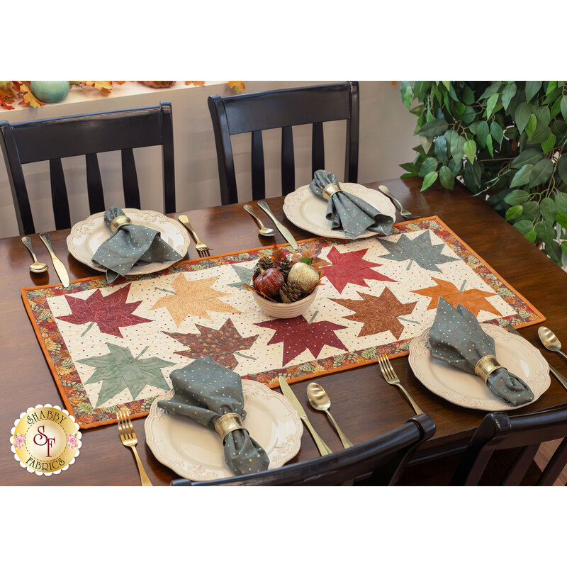 A wooden dining table set with four plates, silverware, and a colorful autumn-themed table runner in the center.