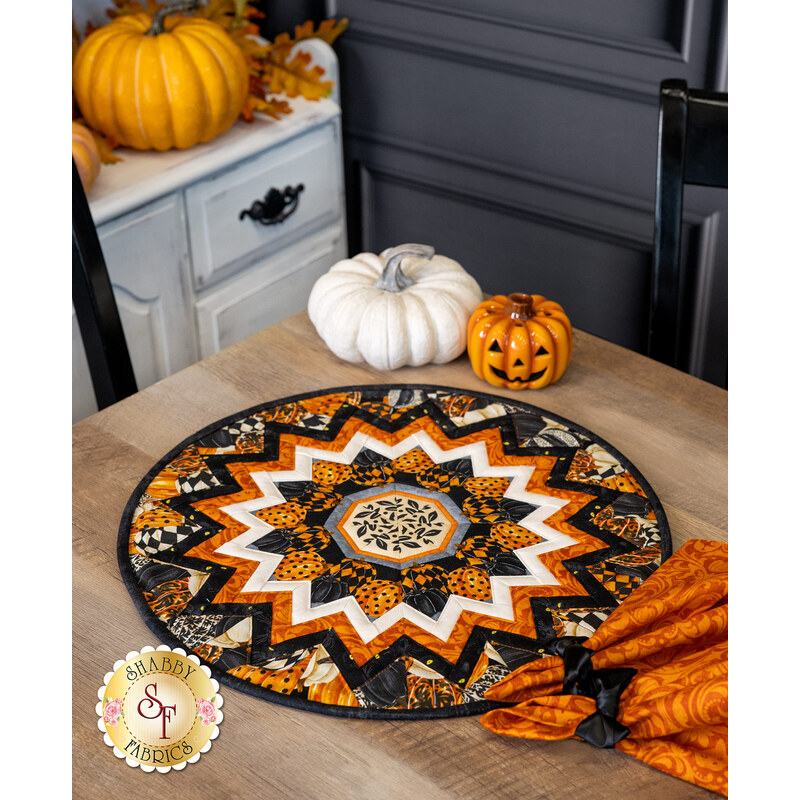 The completed topper quilt in black, white, and orange Halloween fabrics, staged on a wooden table with coordinating decor.