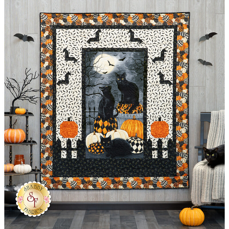 A Halloween-themed quilt featuring black cats, pumpkins, and bats, displayed in a cozy room.