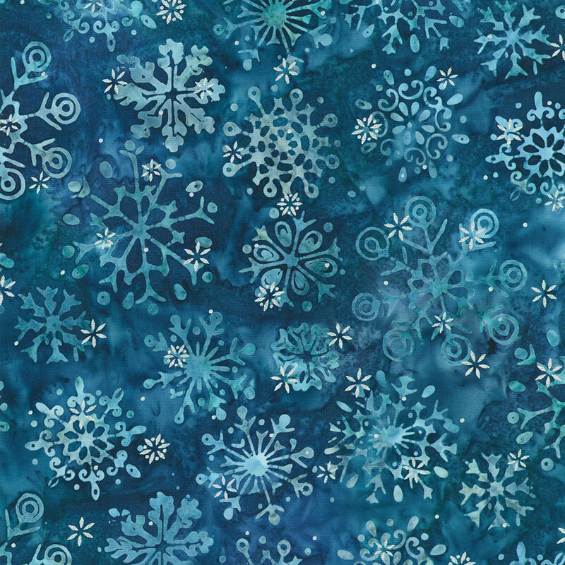 Batik fabric with various blue and white snowflakes on a dark navy background, creating a winter theme.