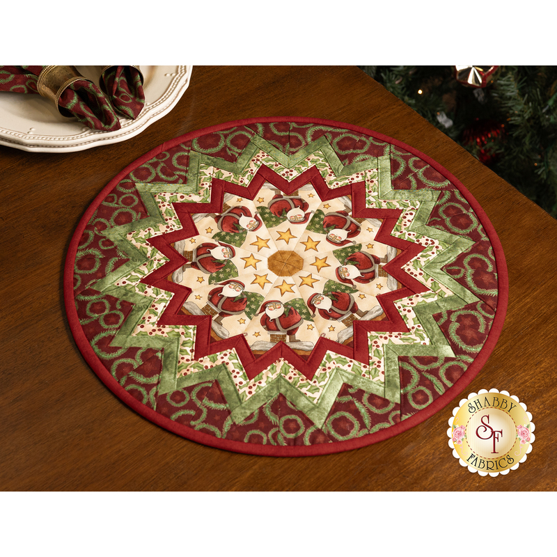 The completed Up On The Housetop Table Topper, colored in red, green, and cream, with coordinating napkins on a plate in the top left corner, staged on a brown table.