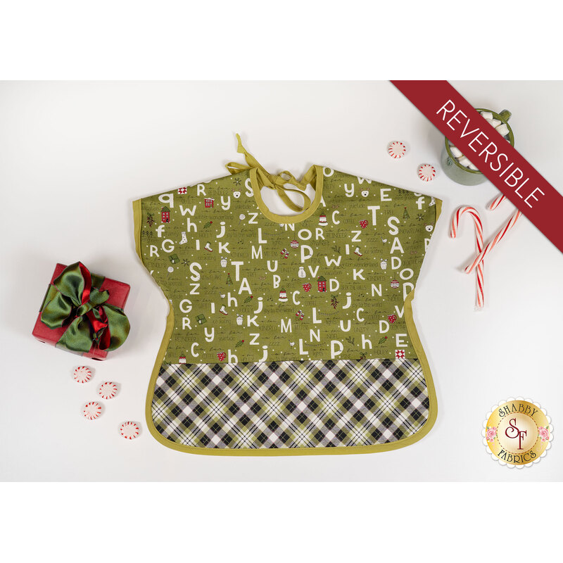 A top down shot of the completed bib in green, isolated on a white background and staged with a coordinating present, candy canes, and a mug with marshmallows.