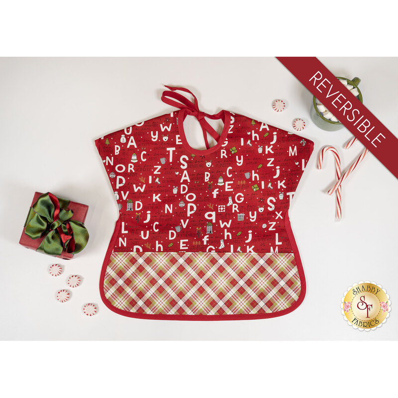 A top down shot of the completed bib in red, isolated on a white background and staged with a coordinating present, candy canes, and a mug with marshmallows.