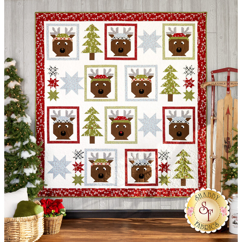 The completed Reindeer Gang Quilt in On Dasher, staged against rustic wood paneling beside matching winter and Christmas decor. 