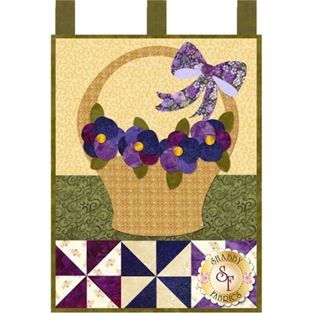 Tan basket filled with purple pansies and decorated with a purple ribbon.