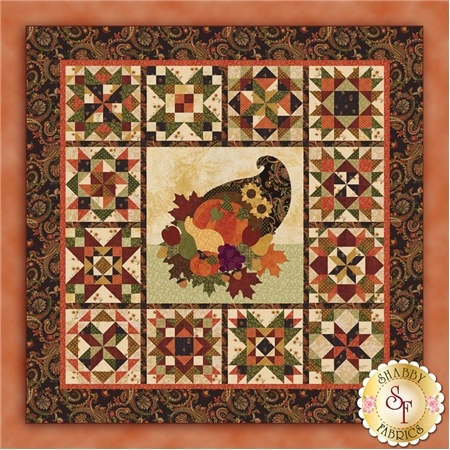 The finished Give Thanks quilt with an applique cornucopia in the center, surrounded by 12 pieced sampler blocks.