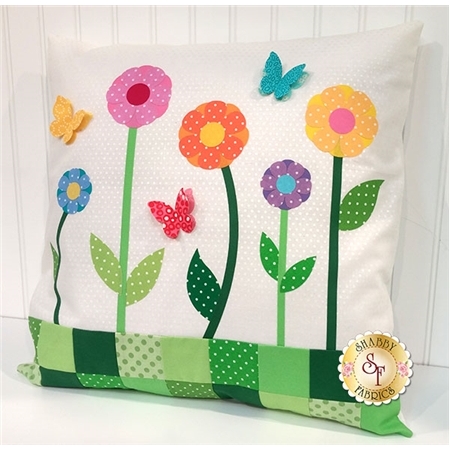 White polka-dotted pillow with colorful flower and butterfly applique shapes.