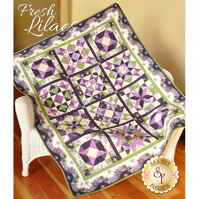 Purple and green pieced geometric quilt spread over a large white wicker chair.