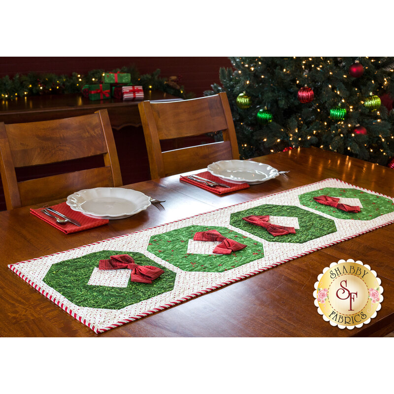 Angled view of a white table runner with red polka dots featuring four patchwork wreaths with bows.