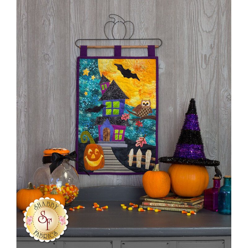 Wall hanging with a spooky mansion, smiling jack-o-lantern, owl, and full moon.