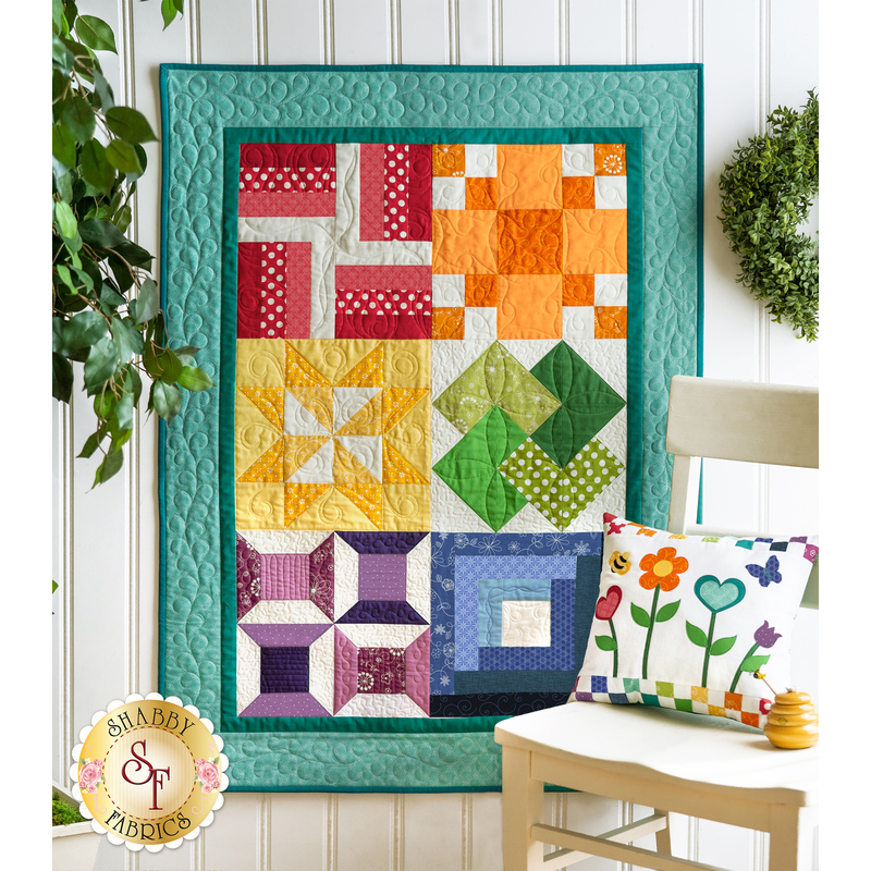 An image of a Learn To Quilt Beginner Quilt hanging on a wall surrounded by greenery.