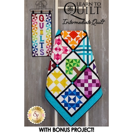 Completed Learn To Quilt Intermediate Quilt Kit draped beside the Quilts Wall Hanging.