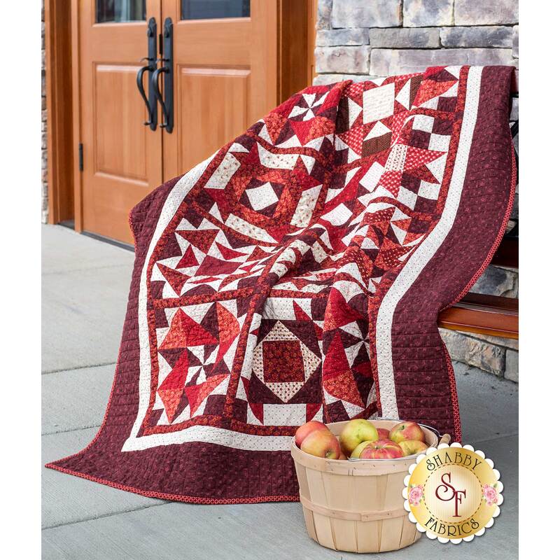Wide shot of red and burgundy patchwork quilt draped over bench.