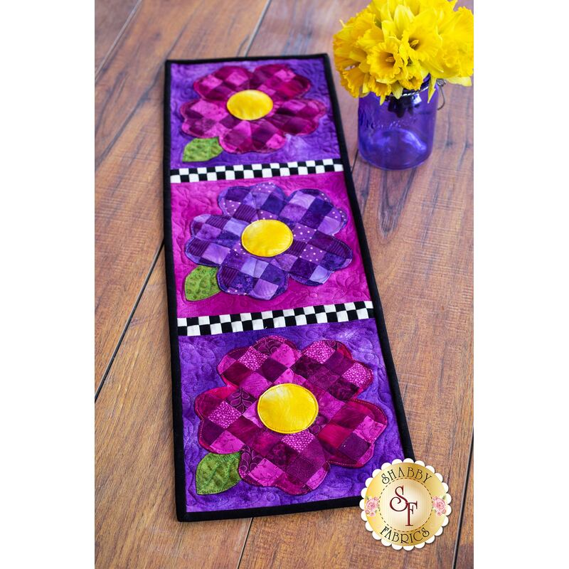 Table runner featuring purple patchwork pansies with yellow centers on purple print backgrounds.
