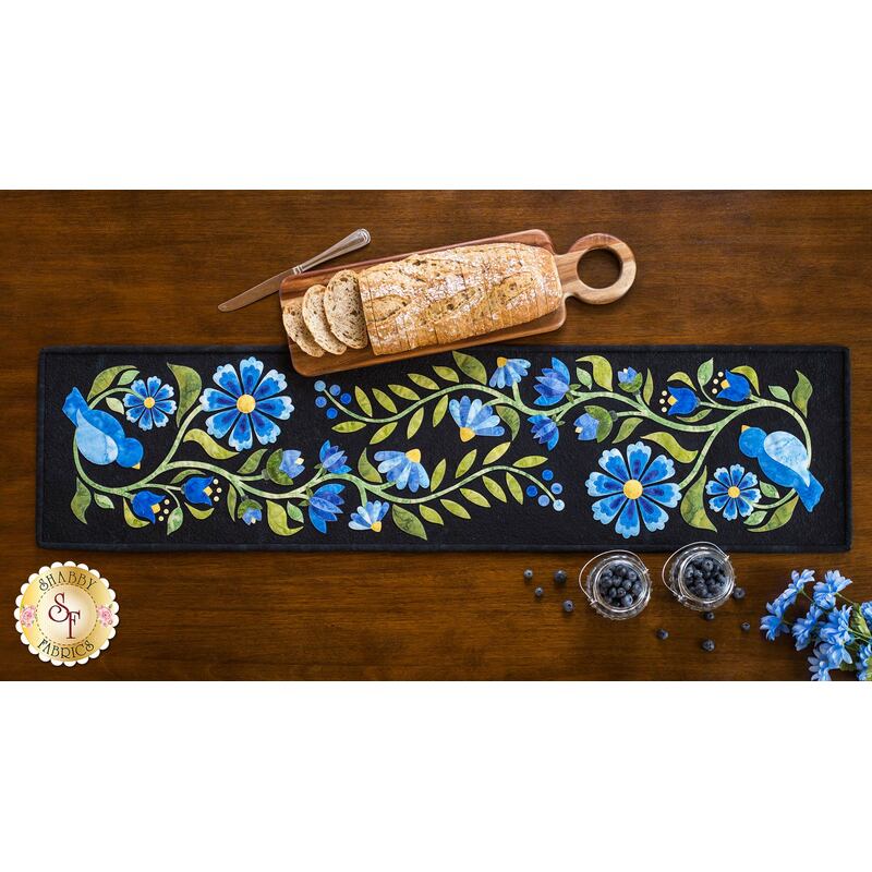 Baltimore-style table runner with blue floral batik applique on black.
