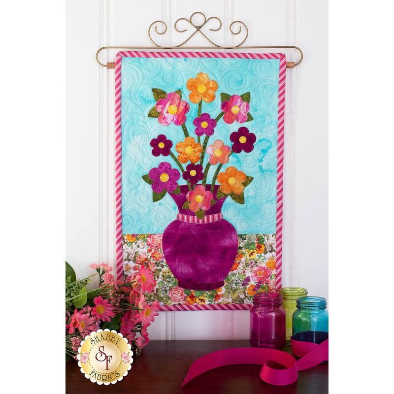 Plum colored vase filled with orange, pink, and purple daises.