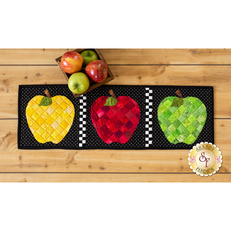 Black background table runner featuring large yellow, red, and green patchwork apples.