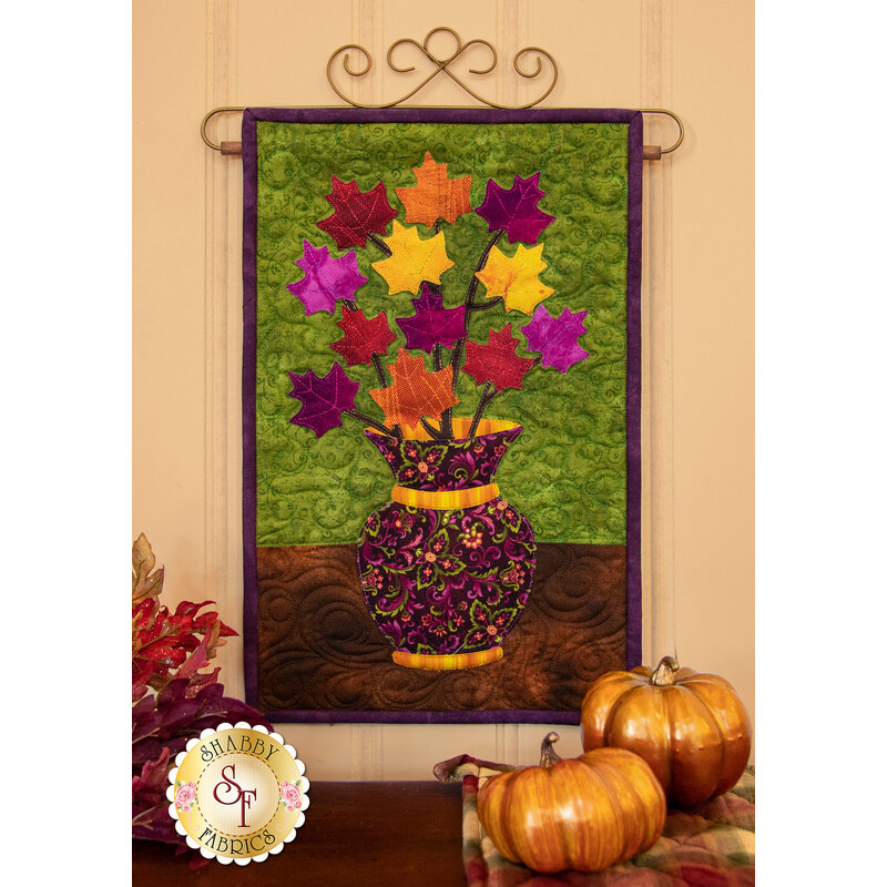 Red, orange, yellow, and purple leaves on branches in a textured purple vase.