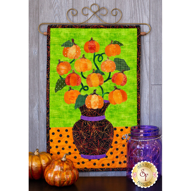 Pumpkins on a curved vine in a black spiderweb vase on a lime green and orange polka-dot background.
