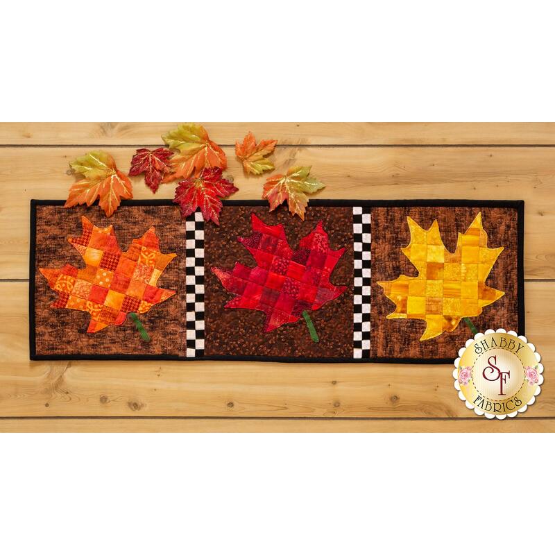 Table runner featuring orange, red, and yellow patchwork maple leaves on brown print backgrounds.