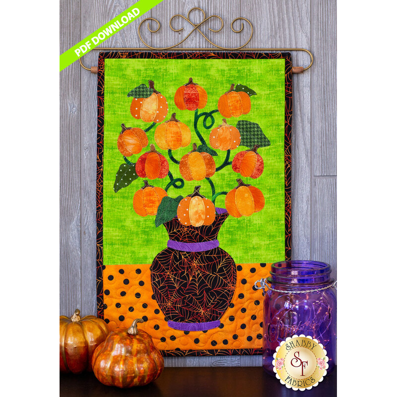 Pumpkins on a curved vine in a black spiderweb vase on a lime green and orange polka-dot background.