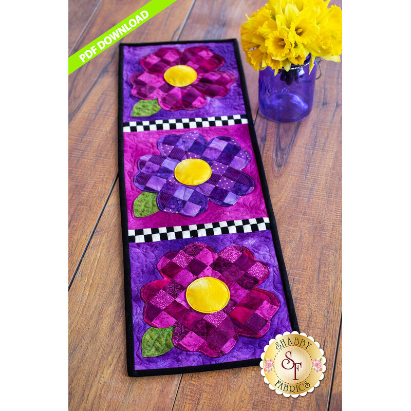 Table runner featuring purple patchwork pansies with yellow centers on purple print backgrounds.