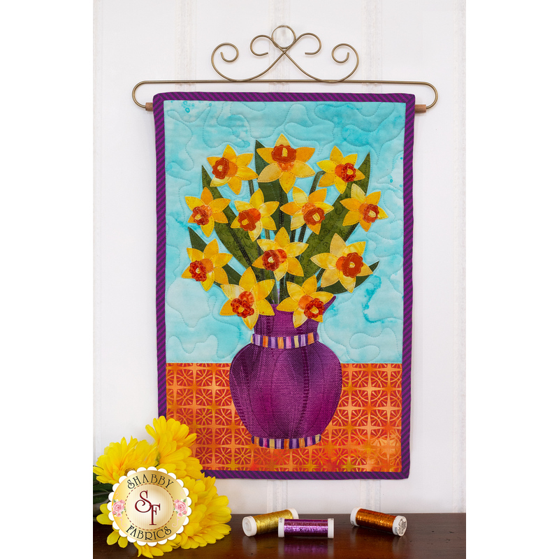 Striped purple vase filled with yellow daffodils on blue background.
