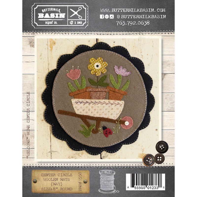 The front of the Center Circle Woolen Mat - May showing the finished mat with three potted flowers in a cute wheelbarrow.