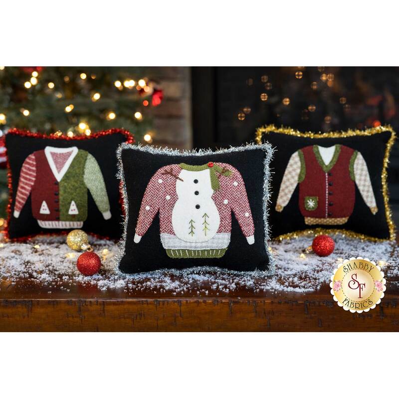 Three ugly sweater pillows displayed on a snow covered table