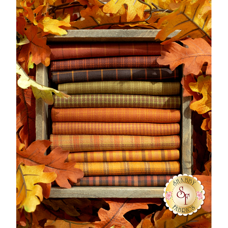 A wooden box holds stacked orange and green fabrics, surrounded by autumn leaves.