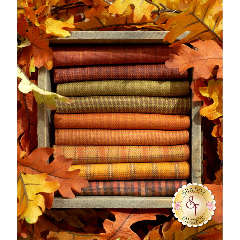 A wooden box holds stacked orange and green fabrics, surrounded by autumn leaves.