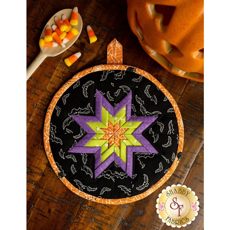 A top down view of a Halloween cloth hot pad displayed on a table with Halloween decor