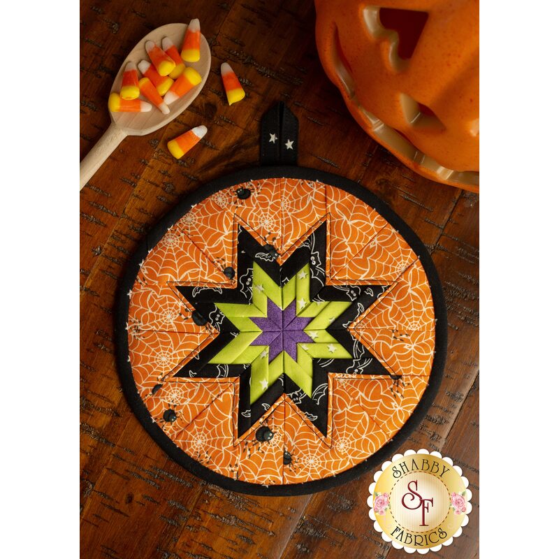 A Halloween spider web themed hot pad on a wood table with Halloween decor