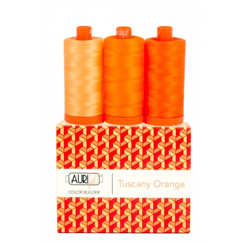 A spool of light, medium, and dark orange thread on an Aurifil Colorbuilder box