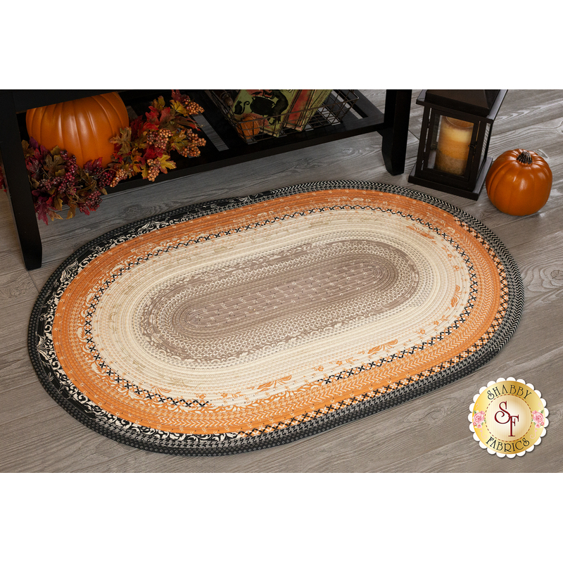 A black, orange, tan, and cream Jelly Roll Rug displayed on a wood floor