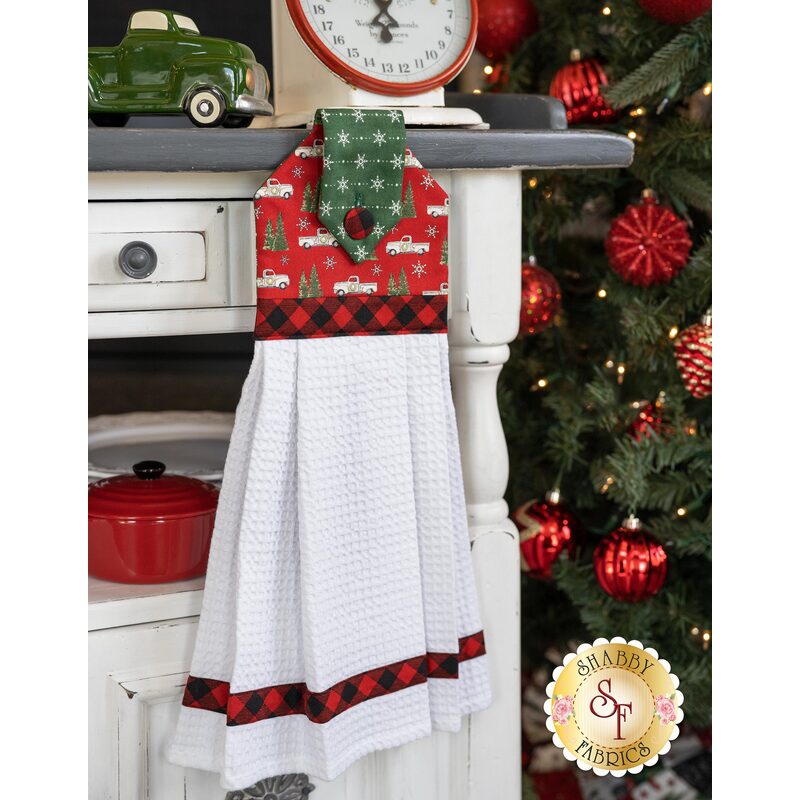 The red and green Christmas themed hanging towel with trucks hung from a cabinet